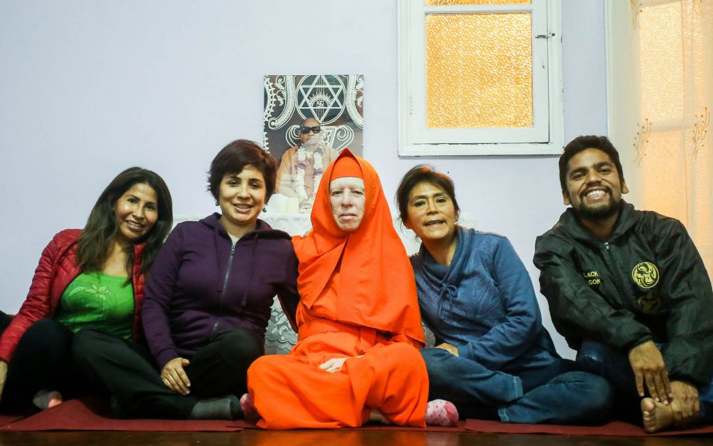 group of 4 Peruvian people sitting on ground with yogic nun wearing orange in the middle